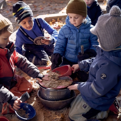 Kids sifting through clay outside over a pot